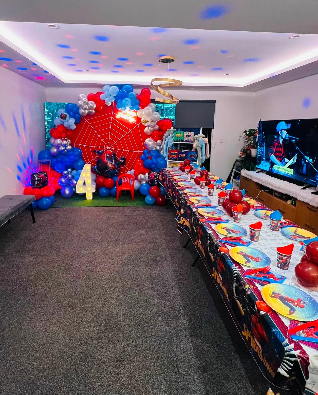 Spider-Man birthday backdrop with a red web arch, balloons, a lit number four and a long party table